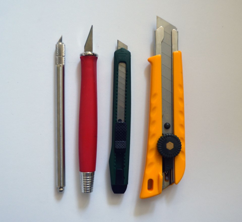 Zwei Skalpelle (links) in unterschiedlichen Größen für die Feinarbeit, ein einfacher Cutter (grün) für größere, gerade Schnitte und ein großer Cutter (gelb) für schwere Materialien wie Graupappe.